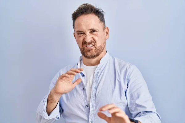 Middle age caucasian man standing over blue background disgusted expression, displeased and fearful doing disgust face because aversion reaction.
