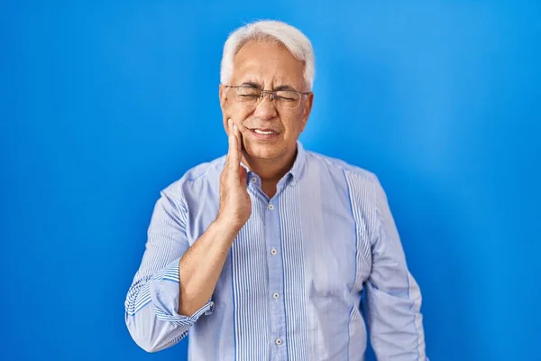 Hispanic senior man wearing glasses touching mouth with hand with painful expression because of toothache or dental illness on teeth. dentist