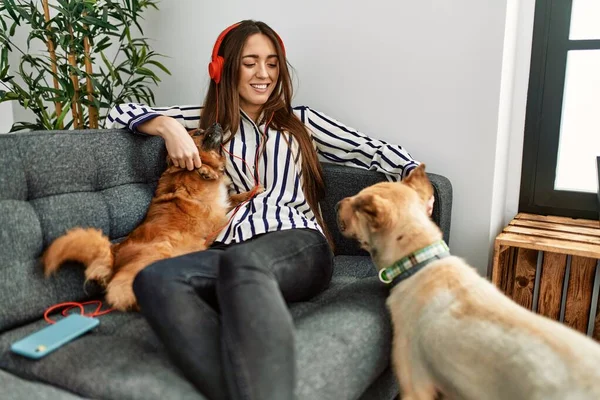 Young hispanic woman listening to music sitting on sofa with dogs at home