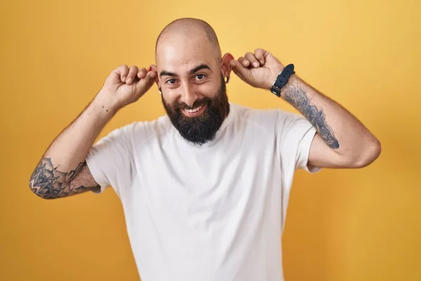 Young Hispanic Man Beard Tattoos Standing Yellow Background Smiling Pulling —  Fotos de Stock