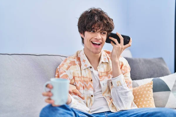 Young Hispanic Man Drinking Coffee Listening Audio Message Smartphone Home — Fotografia de Stock