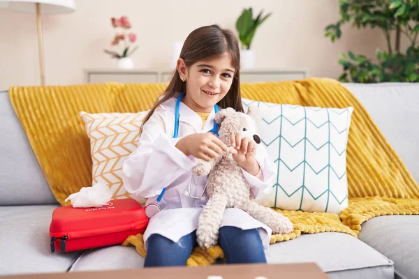 Adorable Hispanic Girl Wearing Doctor Uniform Bandaging Teddy Bear Arm — Zdjęcie stockowe