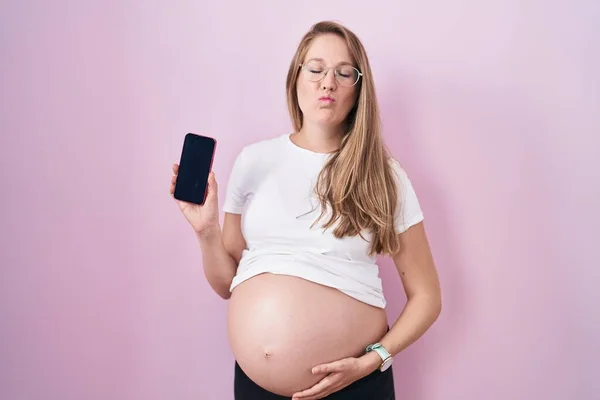 Young Pregnant Woman Showing Belly Holding Smartphone Looking Camera Blowing — Stock fotografie