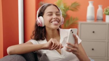 Young african american woman dancing and listening to music sitting on sofa at home