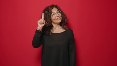 Middle age woman smiling confident doing idea gesture with finger over red background