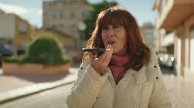 Middle age redhead woman smiling confident sending audio message at street