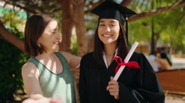 Two women mother and graduated daughter holding diploma kissing at park