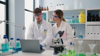 Young couple wearing scientist uniform using laptop at laboratory