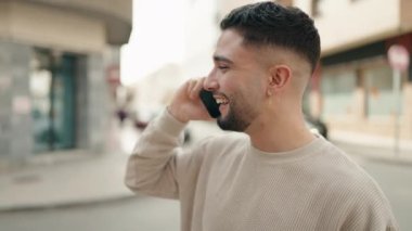 Genç Arap adam gülümsüyor, kendinden emin bir şekilde caddedeki akıllı telefondan konuşuyor.