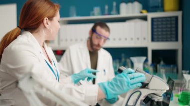 Man and woman scientists using microscope writing on document working at laboratory