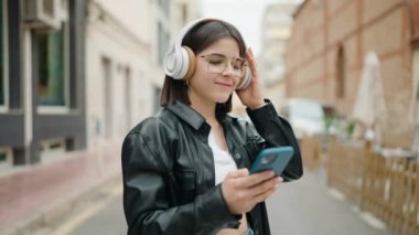 Genç İspanyol kadın sokakta müzik dinlerken kendinden emin gülümsüyor.