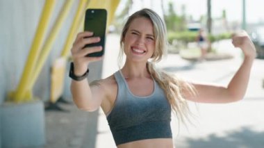 Young blonde woman wearing sportswear make selfie by smartphone at street