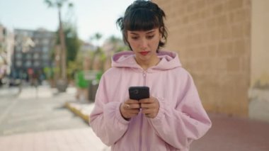 Young hispanic woman surprised using smartphone at street