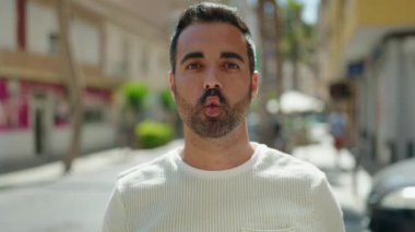 Genç İspanyol adam gülümsüyor. Kendine güveniyor. Dudaklarıyla komik jestler yapıyor.