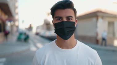 Young hispanic man wearing medical mask standing at street