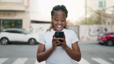 Afro-Amerikalı kadın sokakta akıllı telefon kullanarak kendine güveniyor.
