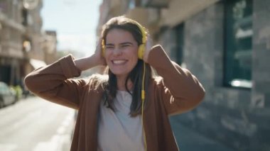 Beyaz bir kadın gülerek sokakta müzik dinliyor.