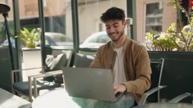 Young hispanic man smiling confident using laptop at coffee shop terrace