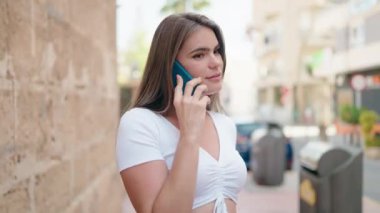 Gülümseyen genç bir kadın caddedeki akıllı telefondan konuşuyor.