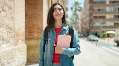 Young hispanic girl student smiling confident holding book walking at street