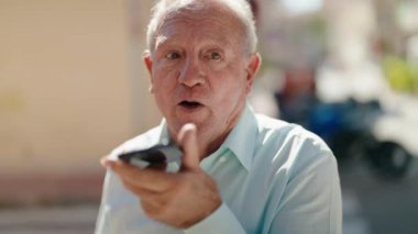 Middle age grey-haired man talking on smartphone with serious expression at street