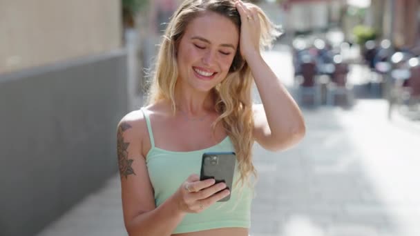 Junge Blonde Frau Lächelt Selbstbewusst Mit Smartphone Auf Der Straße — Stockvideo