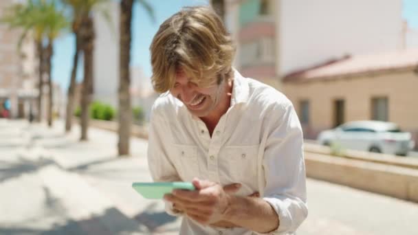 Junger Mann Lächelt Selbstbewusst Und Sieht Video Auf Smartphone Auf — Stockvideo