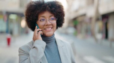 Afro-Amerikalı kadın gülümsüyor. Akıllı telefondan konuşuyor.