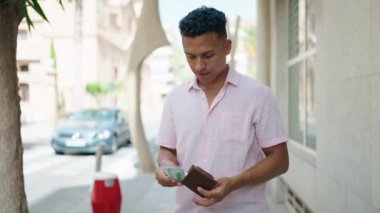 Young latin man smiling confident counting dollars at street
