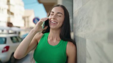 Genç, güzel, İspanyol bir kadın gülümsüyor ve caddede akıllı telefondan konuşuyor.