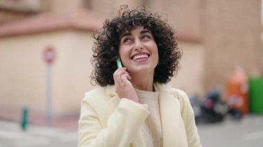 Gülümseyen genç bir kadın caddedeki akıllı telefondan konuşuyor.