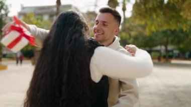 Young couple smiling confident surprise with gift at park