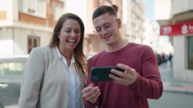 Man and woman mother and son watching video on smartphone at street