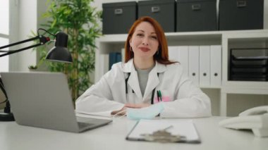 Young redhead woman wearing doctor uniform and medical mask working at clinic