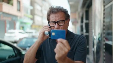 Orta yaşlı bir adam akıllı telefon ve kredi kartıyla konuşuyor.