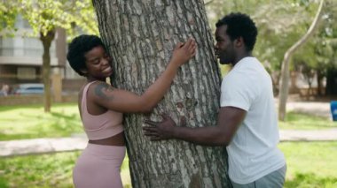 African american man and woman couple hugging tree at park