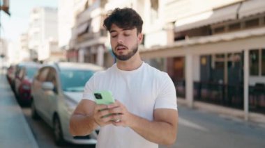 Genç beyaz adam caddedeki akıllı telefondan video görüşmesi yapıyor.