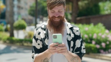 Young redhead man smiling confident using smartphone at park