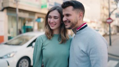 Genç çift gülümsüyor. Birbirlerine sarılıyorlar. Sokakta duruyorlar.