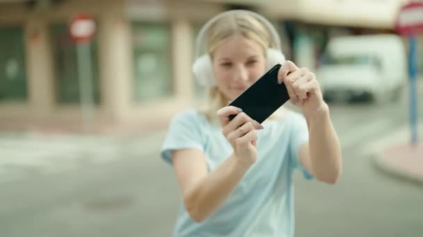 年轻的金发女人笑着自信地在街上玩电子游戏 — 图库视频影像