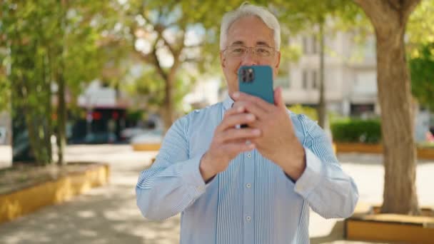 Hombre Mayor Sonriendo Confiado Haciendo Foto Por Teléfono Inteligente Parque — Vídeos de Stock