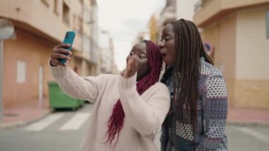 Two african american women smiling confident having video call at street