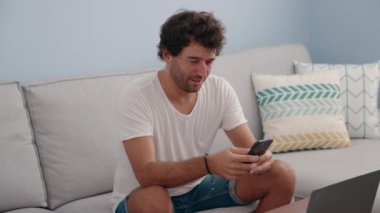 Genç İspanyol adam evde akıllı telefon ve dizüstü bilgisayar kullanıyor.