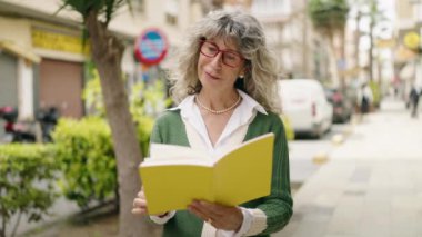 Middle age woman smiling confident reading book at street