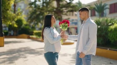 Young latin couple smiling confident suprise with bouquet of roses at park