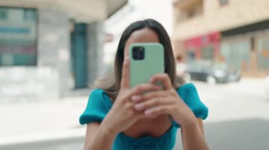 Young hispanic woman smiling confident making photo by the smartphone at street