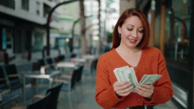 Young redhead woman smiling confident counting dollars at street