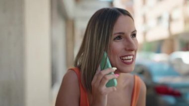 Young blonde woman smiling talking on the smartphone at street