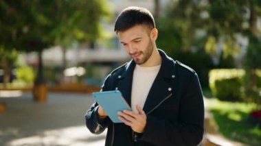 Young hispanic man smiling confident using touchpad at park
