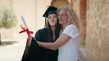 Two women mother and graduated daughter hugging each other at campus university
